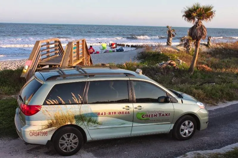 A wrapped Charleston Green Taxi van parked at the beach with the ocean behind it