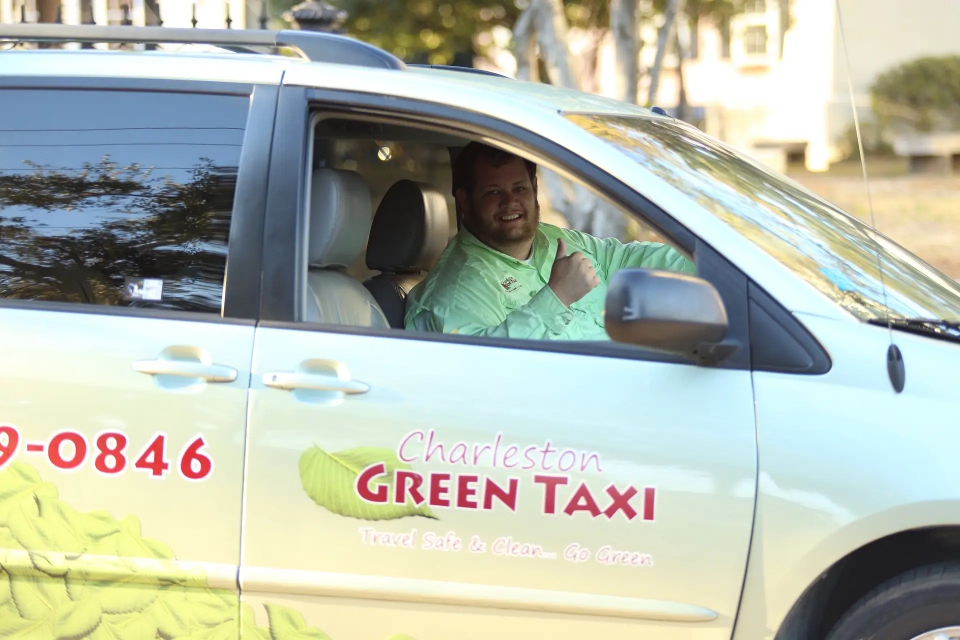 A smiling Charleston Green Taxi driver waving from a wrapped Green Taxi van