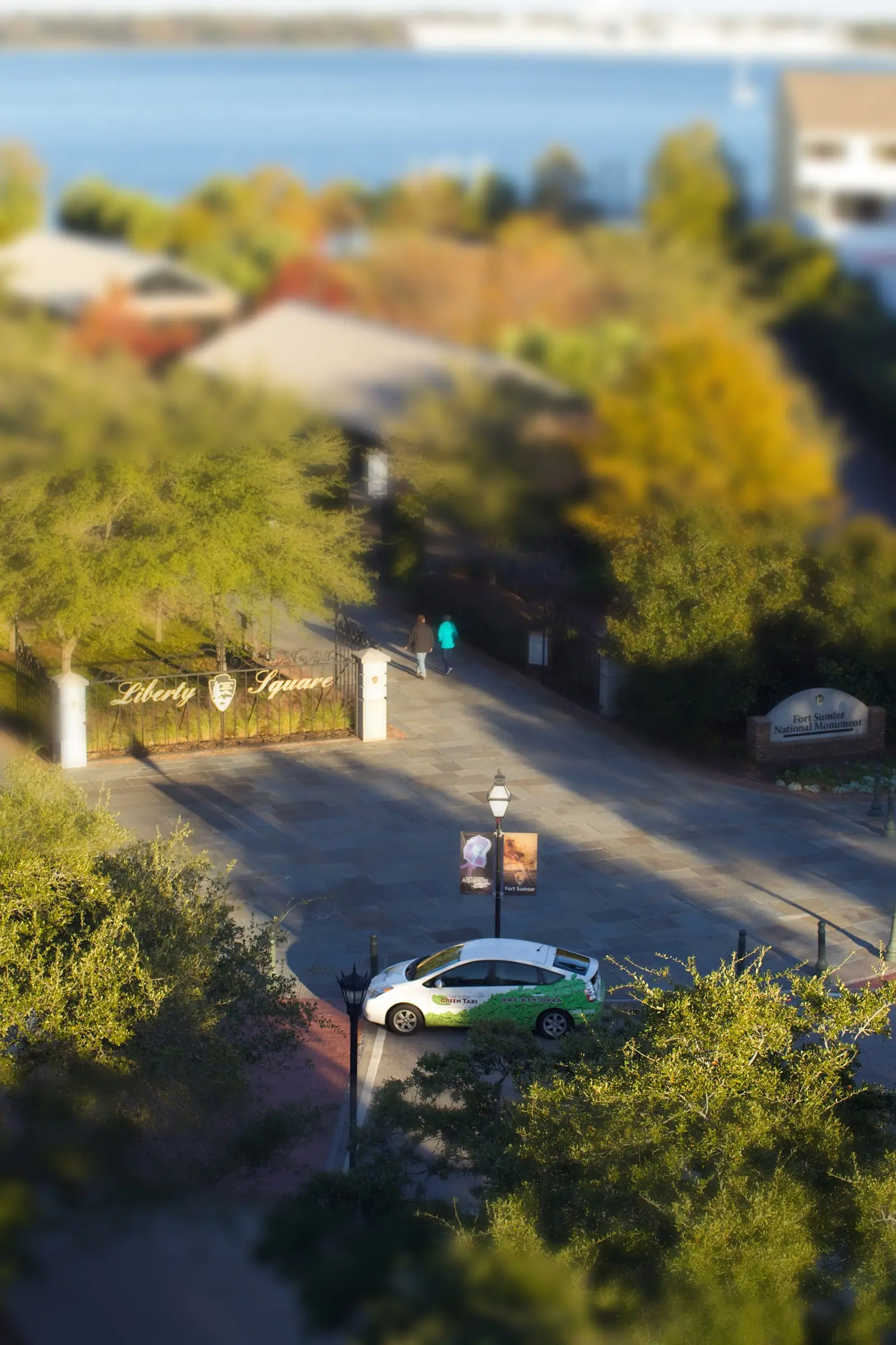 A Green Taxi Prius seen from above at Liberty Square in downtown Charleston, with the harbor behind