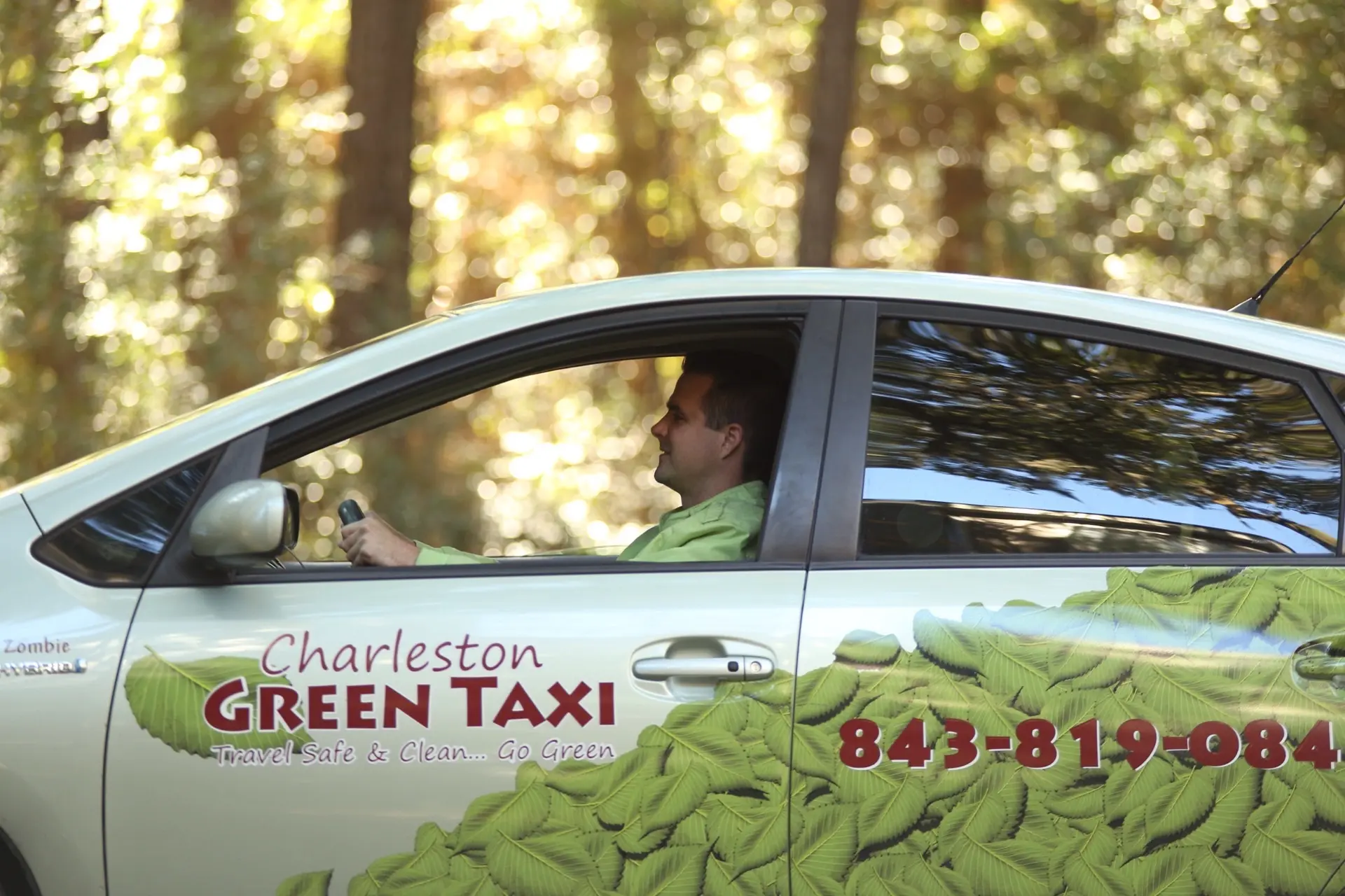 A Charleston Green Taxi driver on the way to a scheduled pickup, leaf-wrapped Prius in motion